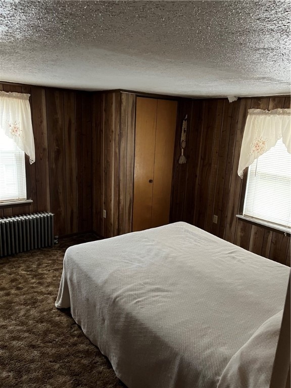 carpeted bedroom featuring a textured ceiling, wooden walls, and radiator