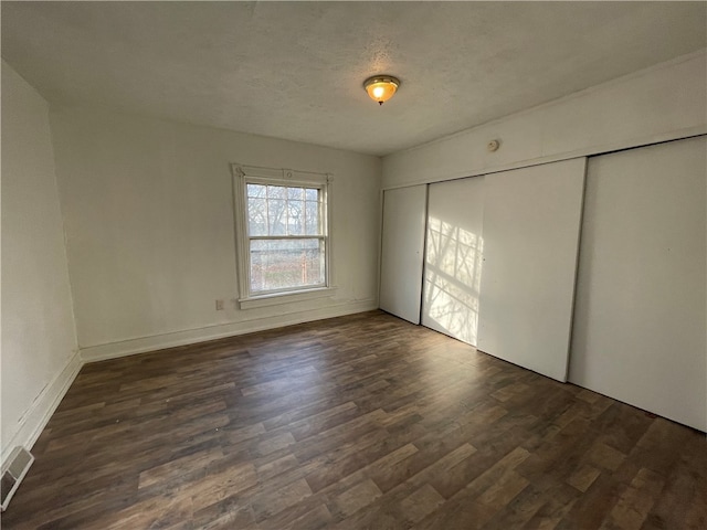 unfurnished bedroom with a textured ceiling, dark hardwood / wood-style floors, and a closet