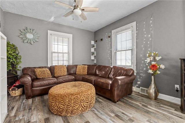 living room featuring ceiling fan, a textured ceiling, light hardwood / wood-style floors, and a healthy amount of sunlight