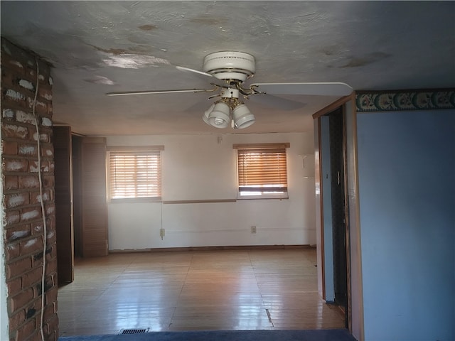 tiled empty room with ceiling fan and brick wall