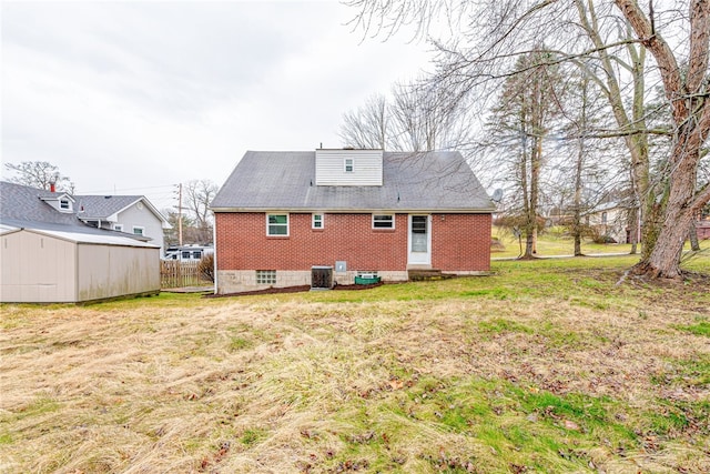 back of house with central AC unit, a storage shed, and a yard