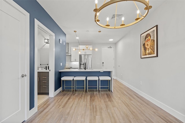 kitchen with stainless steel fridge, light wood-type flooring, white cabinets, and a breakfast bar