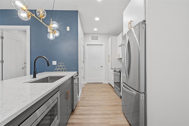 kitchen featuring pendant lighting, light wood-type flooring, stainless steel appliances, sink, and white cabinets