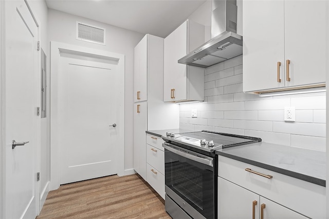 kitchen featuring light wood-type flooring, backsplash, stainless steel electric stove, white cabinetry, and wall chimney exhaust hood