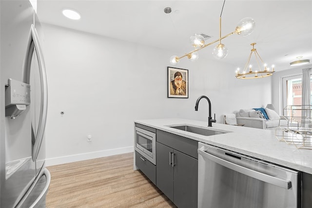 kitchen with pendant lighting, sink, appliances with stainless steel finishes, a notable chandelier, and light wood-type flooring