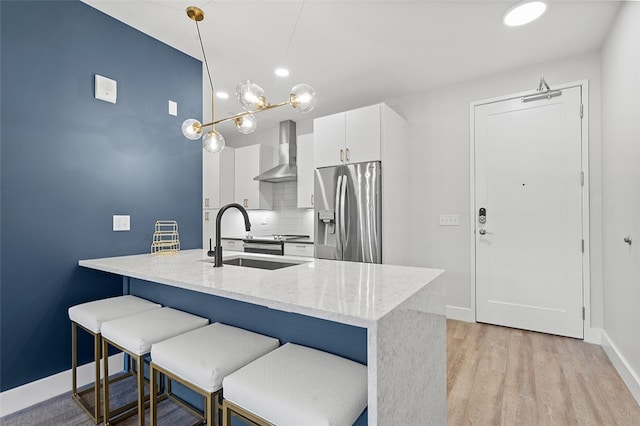 kitchen with stainless steel fridge, light stone counters, white cabinets, light hardwood / wood-style floors, and wall chimney range hood