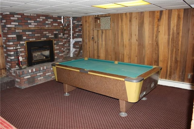 recreation room featuring a drop ceiling, dark colored carpet, a brick fireplace, and billiards