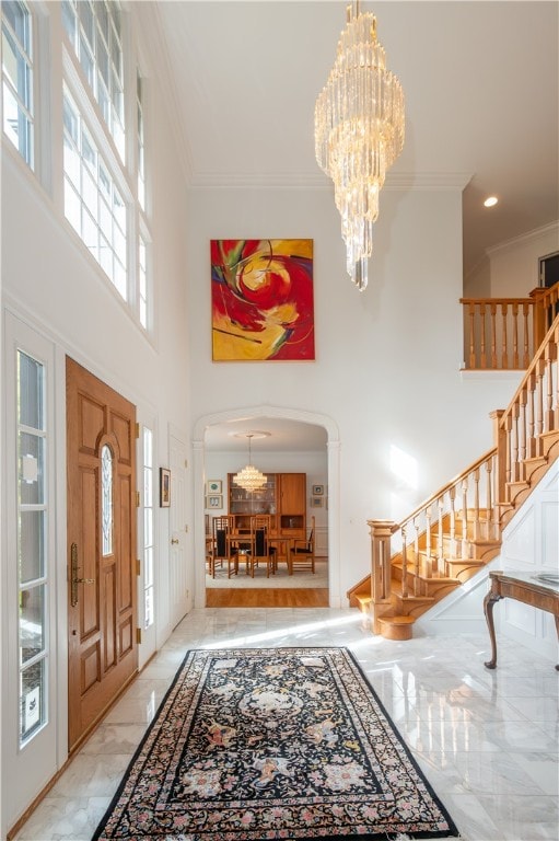 tiled foyer featuring a high ceiling, a notable chandelier, plenty of natural light, and crown molding