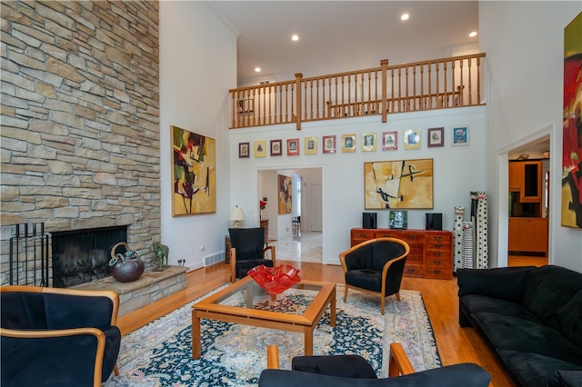 living room with light hardwood / wood-style flooring, a stone fireplace, and a towering ceiling