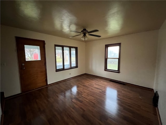 empty room featuring a wealth of natural light, dark wood-type flooring, and ceiling fan