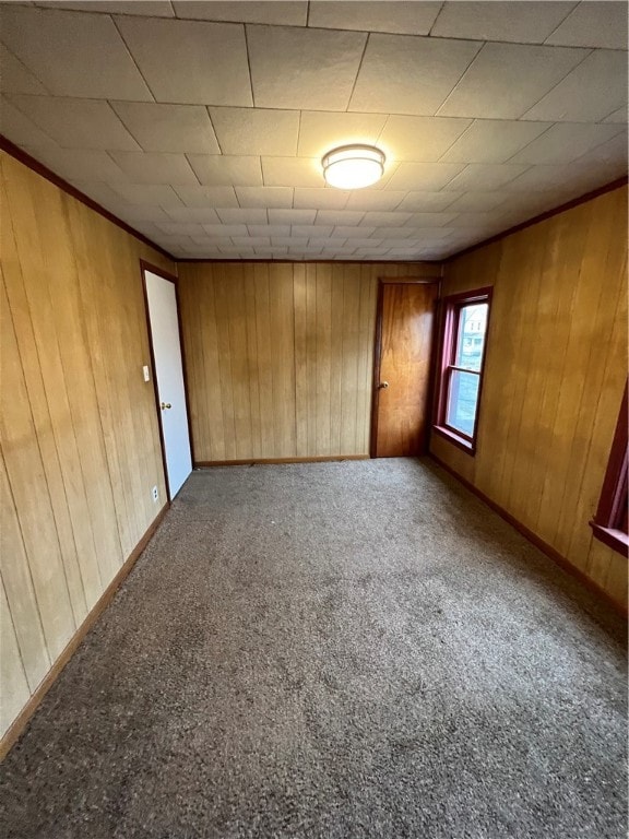 carpeted empty room featuring wooden walls and crown molding