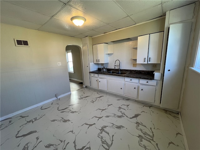 kitchen featuring a drop ceiling, white cabinets, light tile patterned floors, and sink