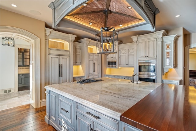 kitchen with dark hardwood / wood-style flooring, a tray ceiling, an island with sink, appliances with stainless steel finishes, and wooden ceiling