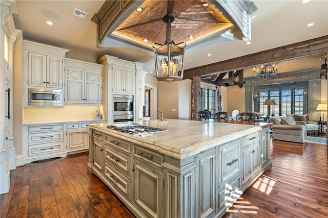 kitchen with appliances with stainless steel finishes, a center island with sink, dark hardwood / wood-style flooring, ceiling fan, and a raised ceiling