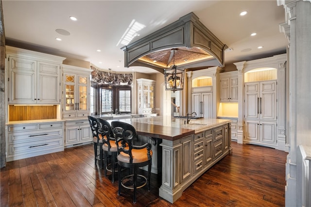 kitchen featuring dark hardwood / wood-style flooring, pendant lighting, dark stone countertops, a kitchen breakfast bar, and a kitchen island with sink