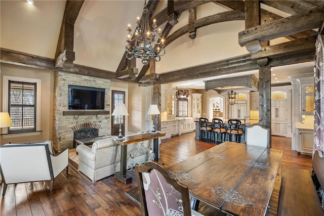 dining space featuring a notable chandelier, a high ceiling, hardwood / wood-style floors, beam ceiling, and a stone fireplace