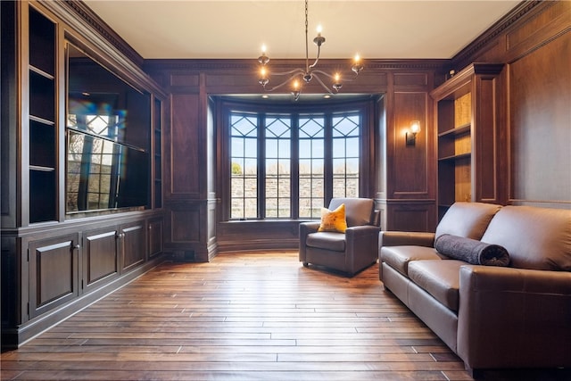 living area with built in features, an inviting chandelier, decorative columns, crown molding, and wood-type flooring