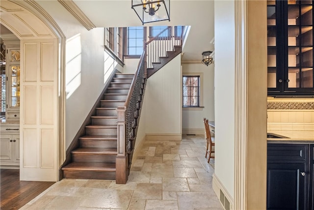 stairway featuring an inviting chandelier, wood-type flooring, and ornamental molding