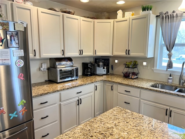 kitchen featuring stainless steel refrigerator, sink, light stone counters, and white cabinetry