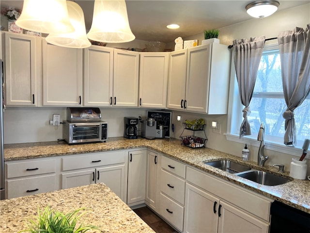 kitchen featuring light stone countertops, decorative light fixtures, sink, white cabinets, and dishwasher