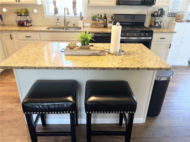 kitchen with light stone counters, white cabinetry, wood-type flooring, sink, and stainless steel gas range oven