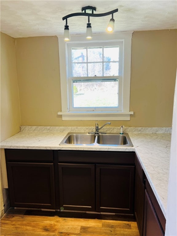 kitchen featuring dark brown cabinets, track lighting, light hardwood / wood-style flooring, and sink