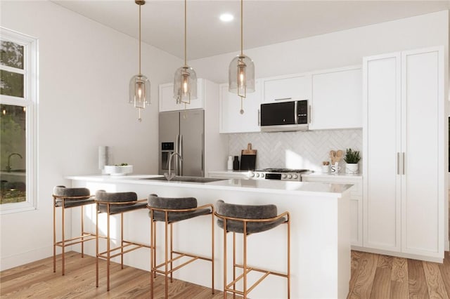 kitchen with sink, light hardwood / wood-style floors, a breakfast bar area, white cabinets, and appliances with stainless steel finishes