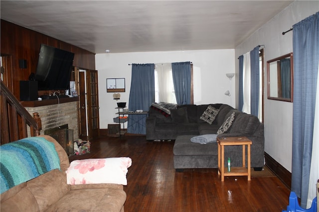 living room with wood walls, a brick fireplace, and dark wood-type flooring