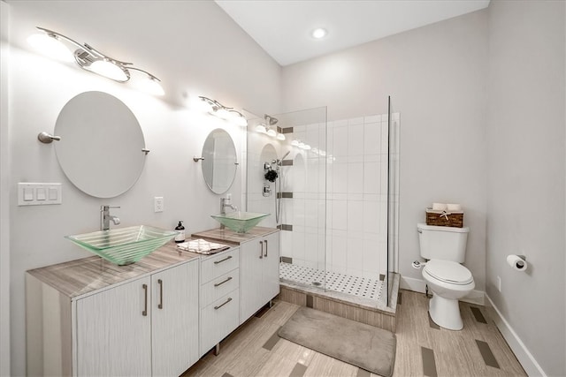 bathroom featuring hardwood / wood-style floors, tiled shower, toilet, and dual bowl vanity