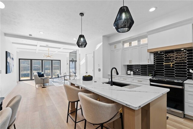 kitchen with coffered ceiling, decorative light fixtures, tasteful backsplash, white cabinetry, and stainless steel range