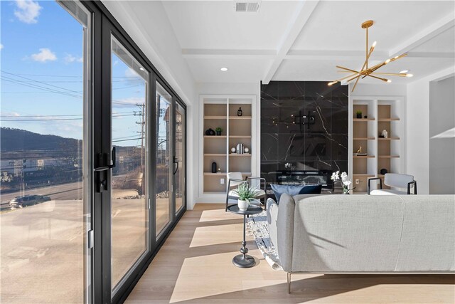 living room featuring plenty of natural light, beamed ceiling, a notable chandelier, and light hardwood / wood-style flooring