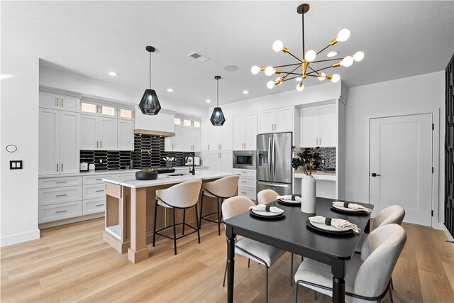 interior space featuring backsplash, a center island with sink, decorative light fixtures, and appliances with stainless steel finishes