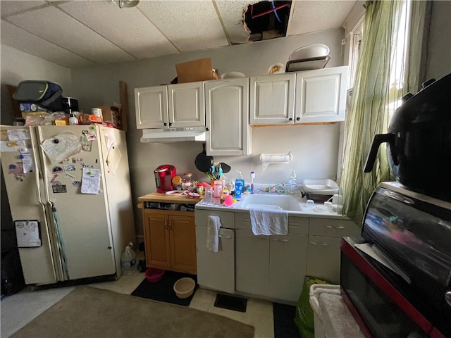 kitchen with a drop ceiling, white cabinetry, white fridge, and sink