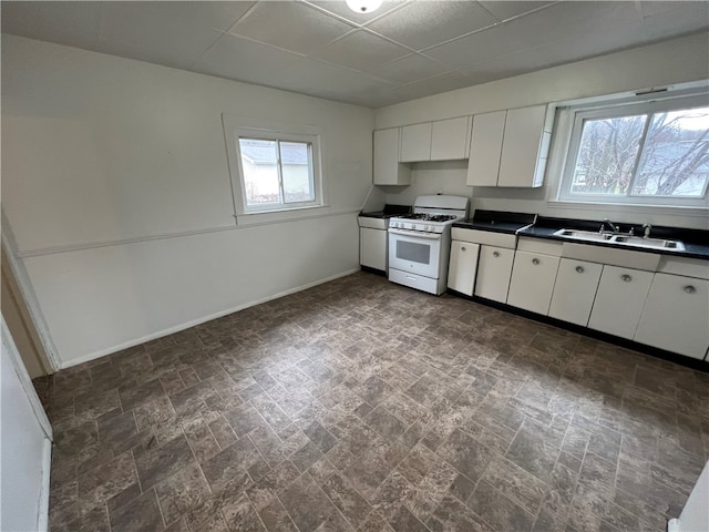 kitchen featuring white gas stove, sink, plenty of natural light, and white cabinets