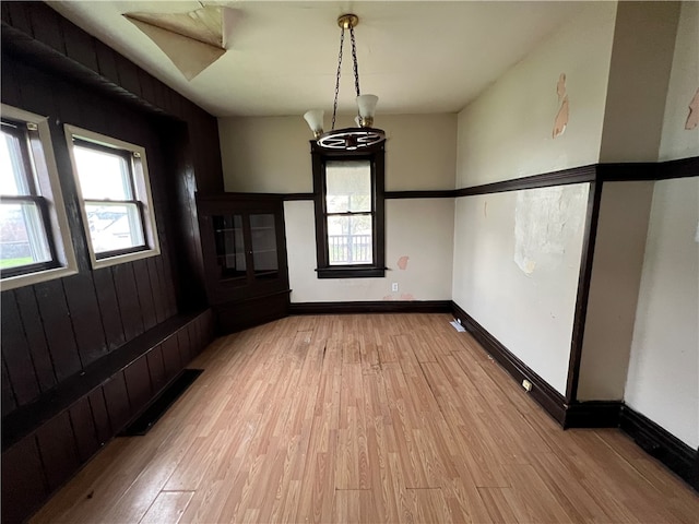 unfurnished dining area featuring an inviting chandelier and light hardwood / wood-style flooring