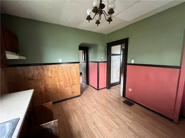 interior space with light hardwood / wood-style floors, an inviting chandelier, and wood walls