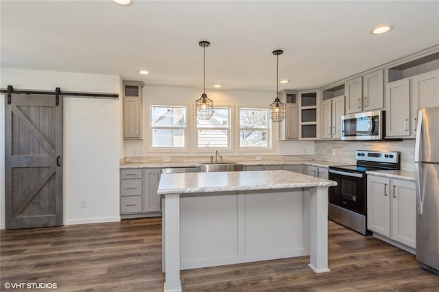 kitchen with dark wood-type flooring, stainless steel appliances, a center island, a barn door, and decorative light fixtures