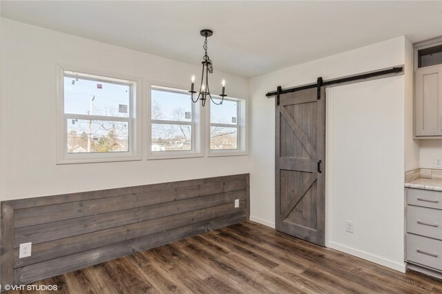 unfurnished dining area featuring a barn door, a notable chandelier, and dark hardwood / wood-style flooring