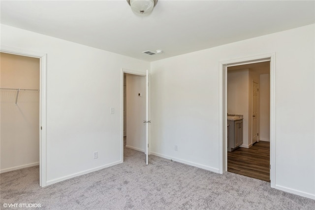 unfurnished bedroom with light carpet, a walk in closet, a closet, and ensuite bathroom