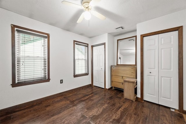 unfurnished bedroom with ceiling fan, two closets, dark hardwood / wood-style floors, and a textured ceiling