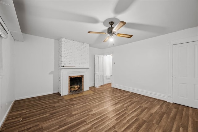 unfurnished living room featuring brick wall, a brick fireplace, dark hardwood / wood-style flooring, and ceiling fan