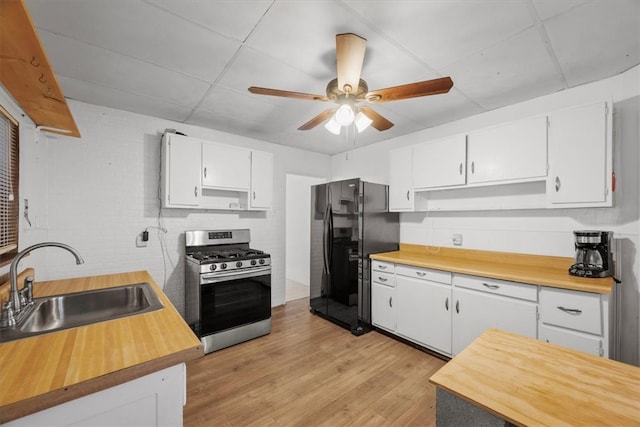 kitchen with ceiling fan, stainless steel gas range, white cabinets, black fridge, and a drop ceiling