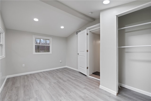 unfurnished bedroom with a closet, vaulted ceiling with beams, and light hardwood / wood-style floors