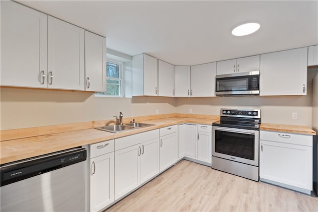 kitchen with light hardwood / wood-style floors, white cabinets, stainless steel appliances, and wooden counters