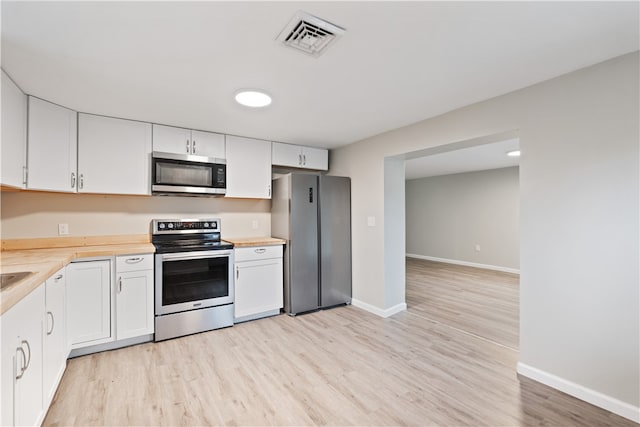 kitchen featuring appliances with stainless steel finishes, light wood-type flooring, butcher block counters, and white cabinetry