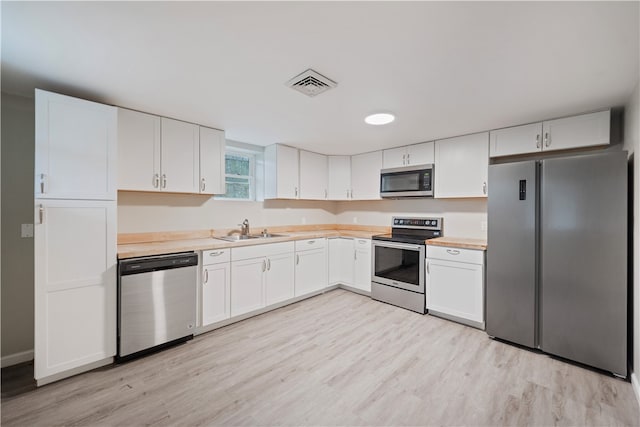 kitchen with appliances with stainless steel finishes, light wood-type flooring, white cabinetry, and sink