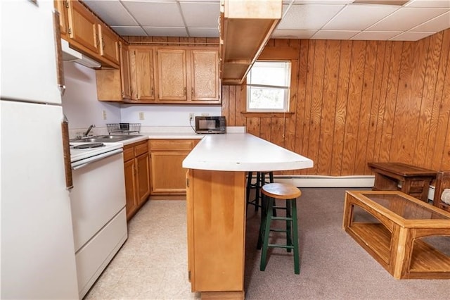 kitchen with a paneled ceiling, white appliances, a breakfast bar area, and baseboard heating