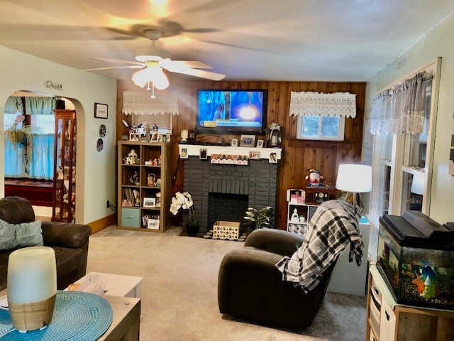 living room with light carpet, a brick fireplace, wooden walls, and ceiling fan