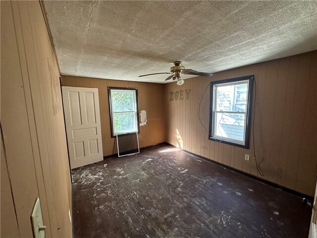 unfurnished room featuring plenty of natural light, a textured ceiling, wooden walls, and ceiling fan