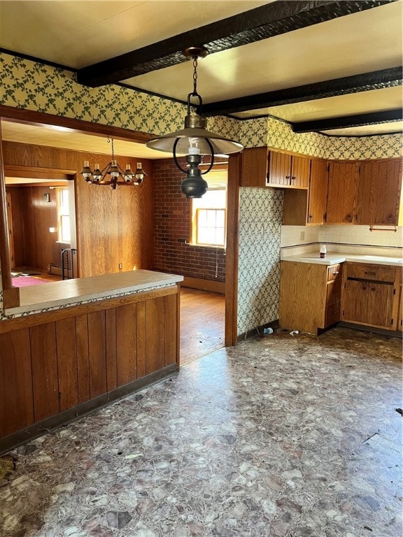 kitchen featuring an inviting chandelier, beamed ceiling, dark tile floors, brick wall, and hanging light fixtures